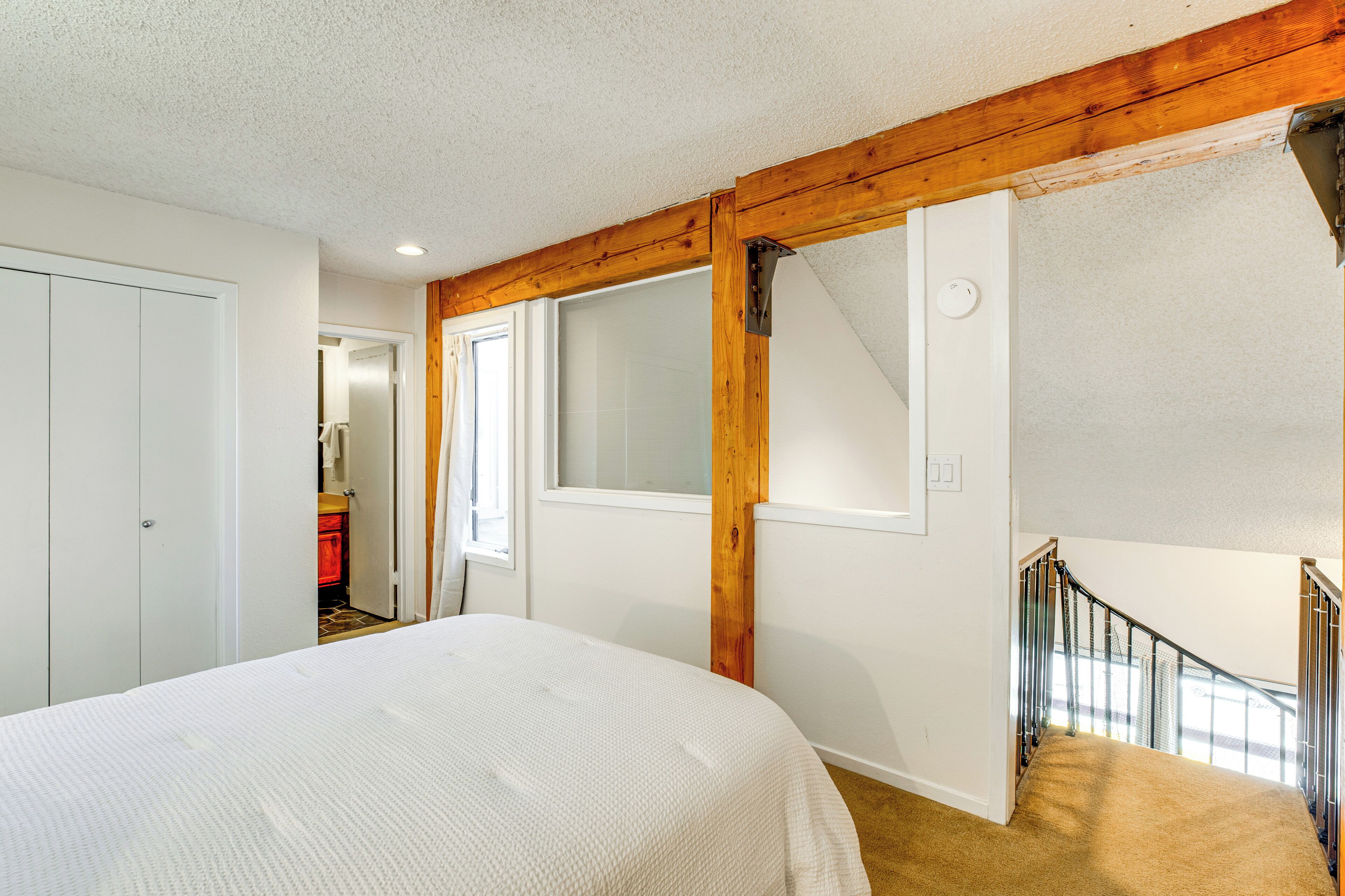 Une chambre avec un grand lit, des poutres en bois, une fenêtre et un escalier.