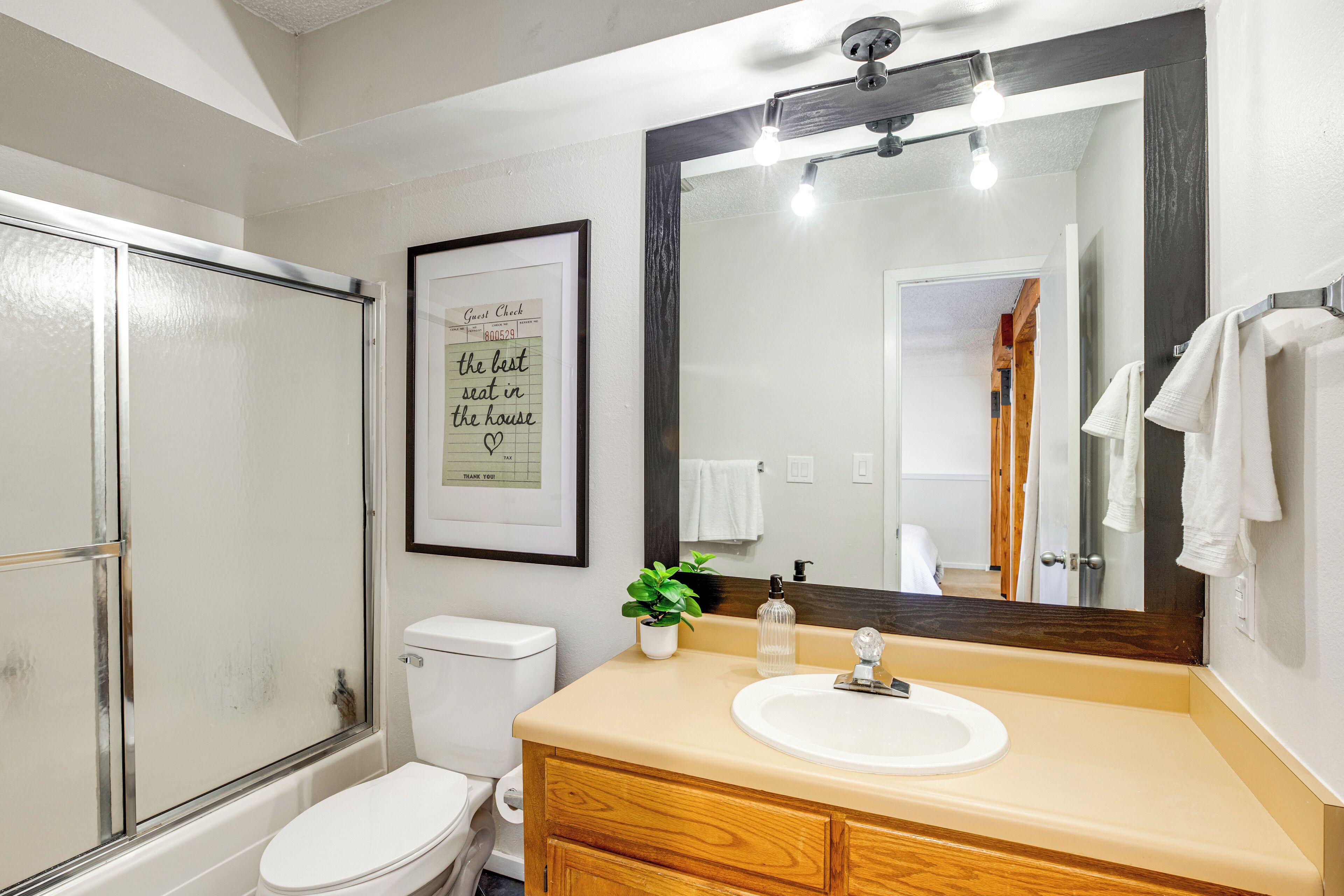 Un baño con ducha, inodoro, lavabo y un espejo grande.