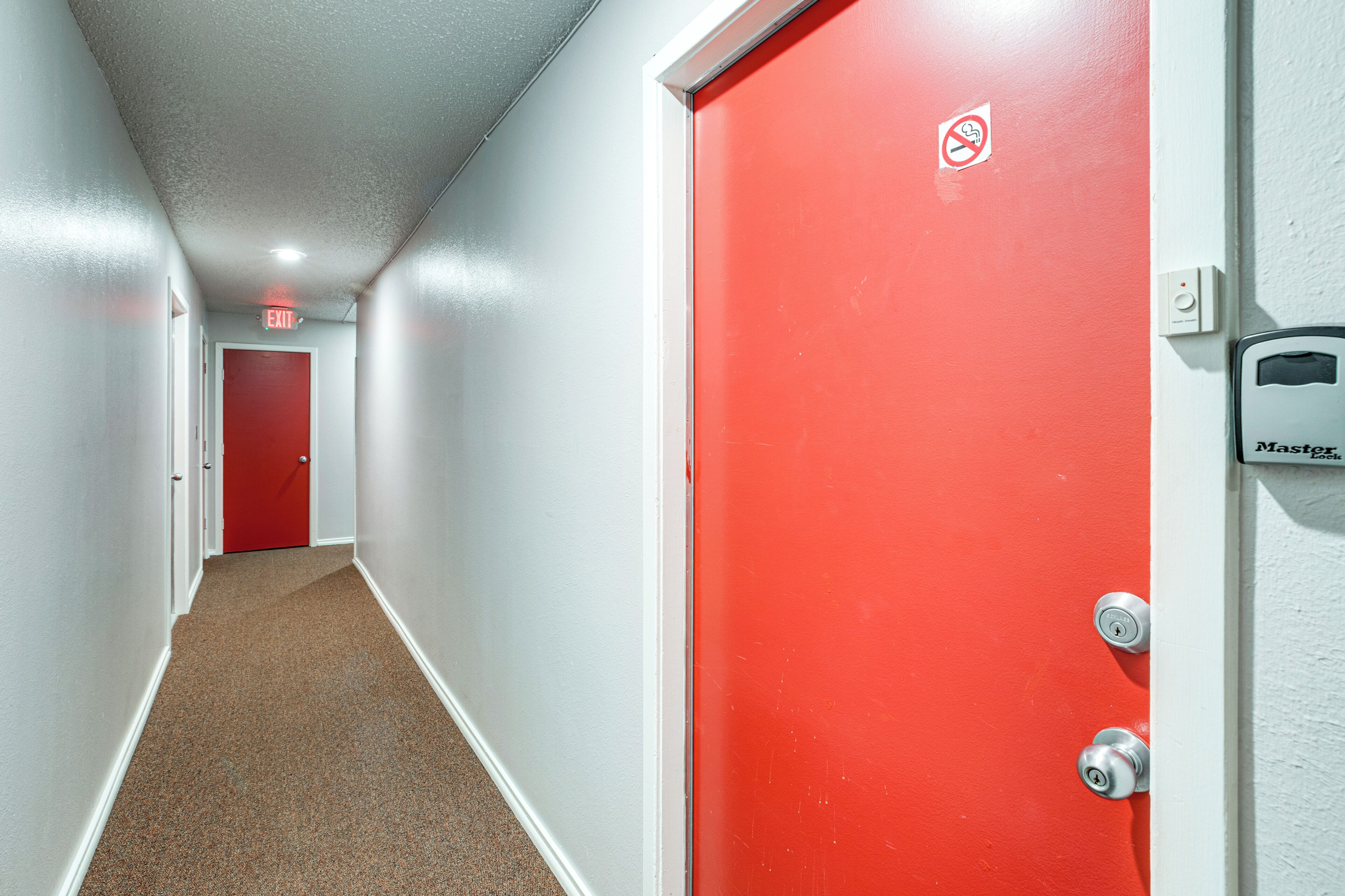 A corridor with a red door, a white door, and an exit sign.