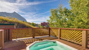 Eine Holzterrasse mit Whirlpool, Holzlattenzaun und einem Berg im Hintergrund.