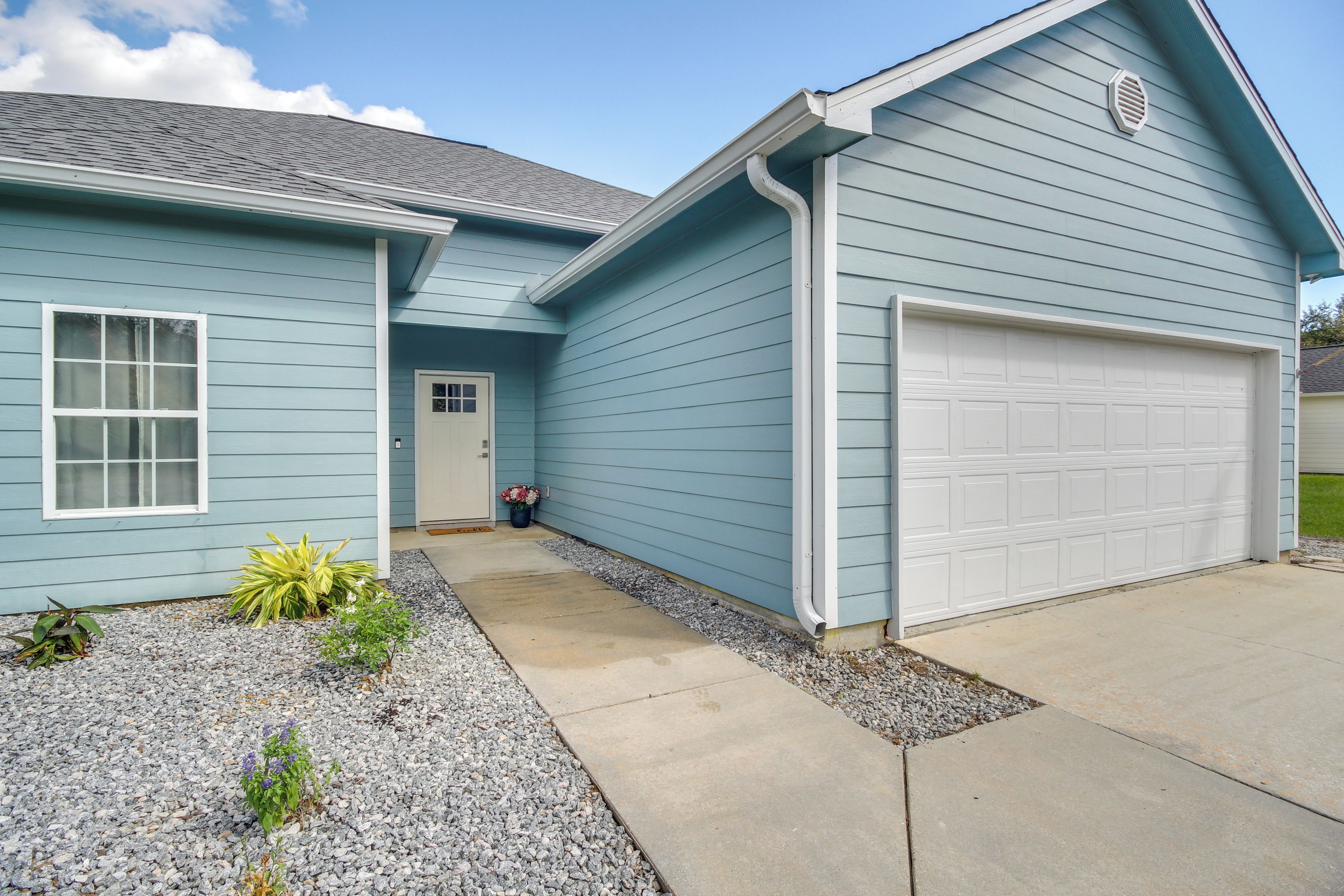 A light blue single-story house with a white garage door, a front door, and a small garden area with gravel and plants.