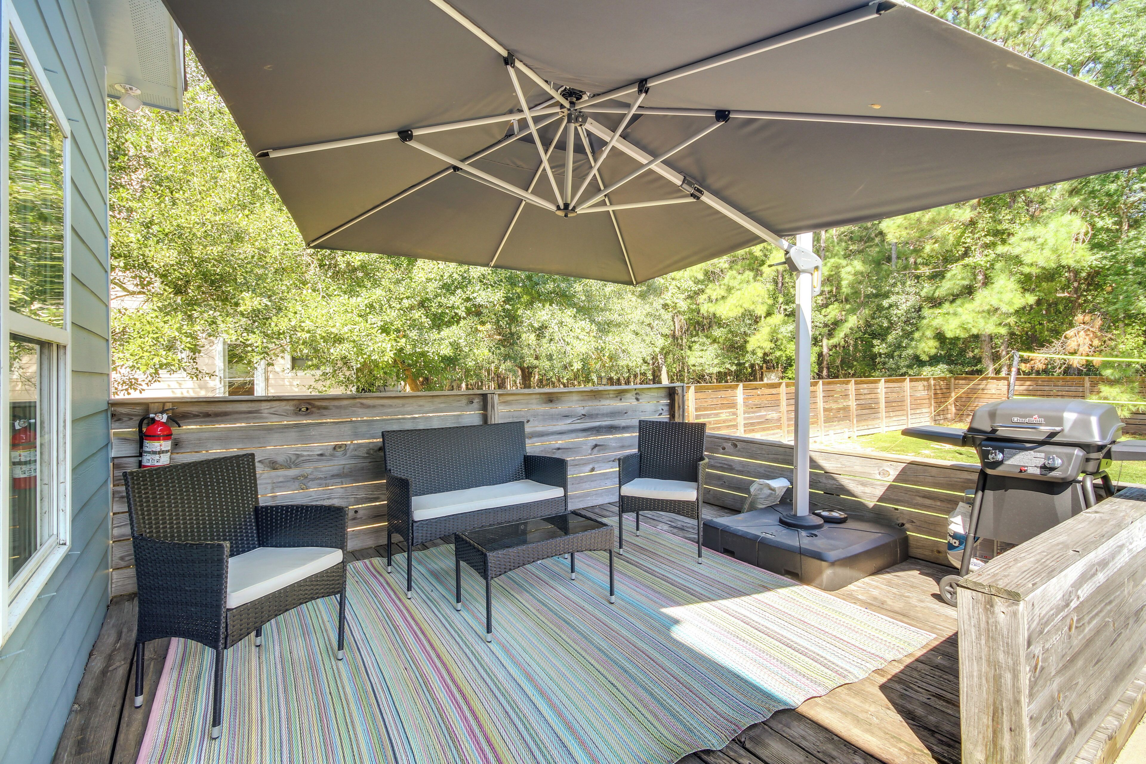 Eine Außenpatio mit einem großen Sonnenschirm, Korbmöbeln, einem Grill und einer Holzterrasse.