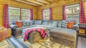 A cozy cabin interior with a sectional sofa, ottoman, and a wooden ceiling.