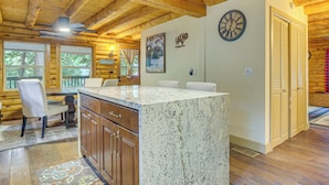 A wooden cabin interior with a kitchen area featuring a granite island, wooden cabinets, and a dining table with chairs.