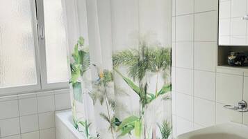 A bathroom with a bathtub, a window with frosted glass, and a shower curtain with a tropical leaf pattern.