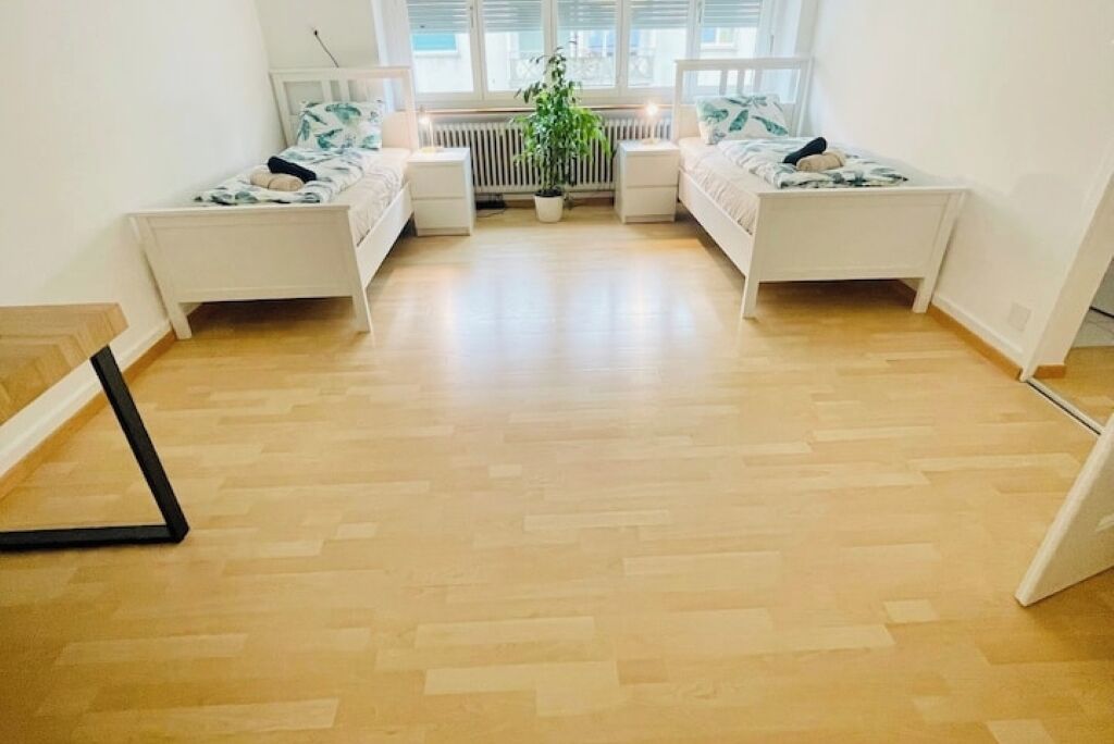 Un dormitorio con dos camas individuales, un radiador, una planta en maceta y una ventana con persianas.