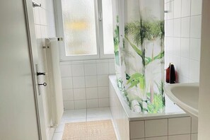 Ein Badezimmer mit Dusche, Badewanne und einem Fenster mit Milchglas.