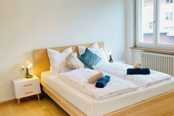 Ein Doppelbett mit weißer Bettwäsche, ein Holzkopfstück und ein Nachttisch mit Lampe.