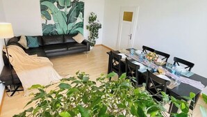 Un salon avec un canapé noir, une table à manger dressée pour quatre personnes et une grande fresque murale.