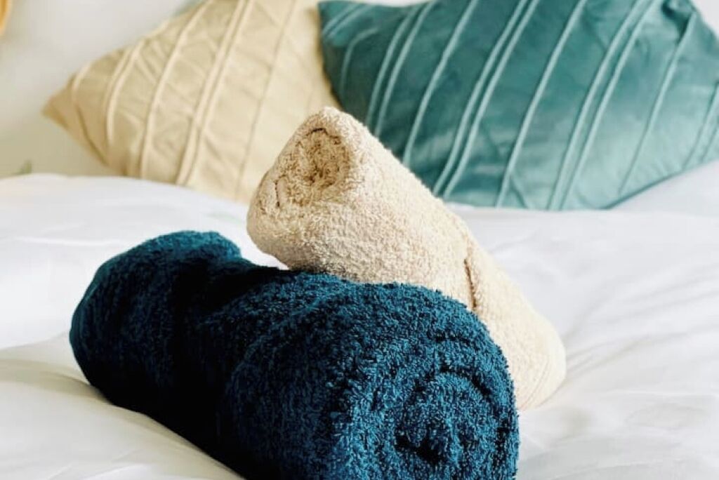 Un lit avec une couverture beige et une couverture bleu foncé, et deux oreillers en arrière-plan.