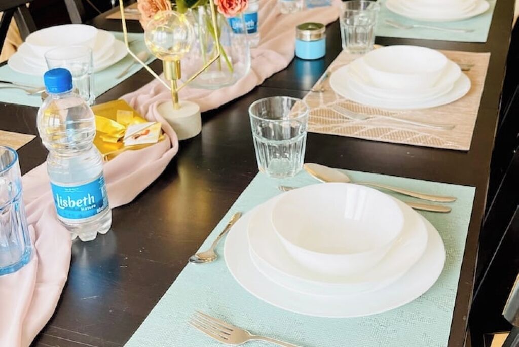A table set with white plates, cutlery, and a water bottle.