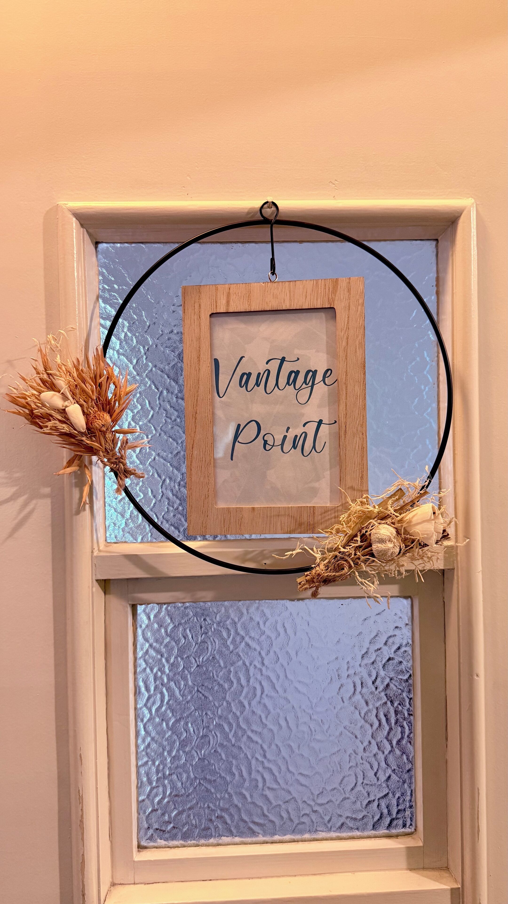 A framed sign with the text "Vantage Point" hanging on a window with a textured glass pane.