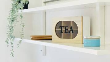 A shelf with a wooden block displaying the word "TEA," a small blue container, and a hanging plant.