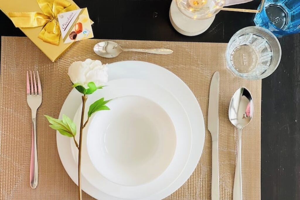 A table set with white plates, silverware, and a small gift box.