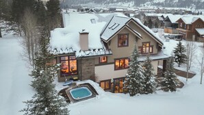 Een chalet bedekt met sneeuw, met een jacuzzi en een zwembad, omringd door bomen en bergen.