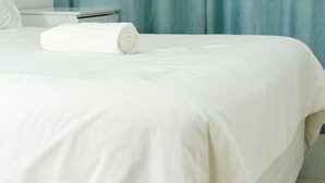 Ein ordentlich bezogenes Bett mit weißer Daunendecke und einem aufgerollten weißen Handtuch.