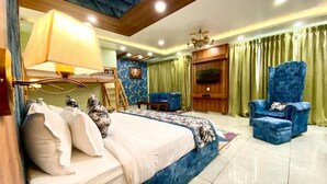A bedroom with a bed, a chair, a TV, and a lamp.
