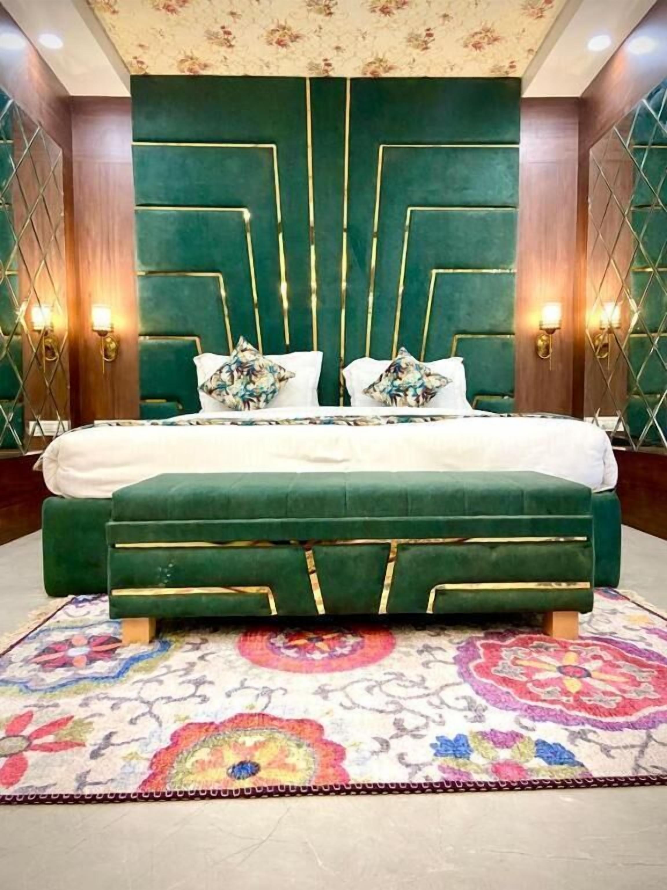 A bedroom with a large bed, green upholstered headboard, and a patterned rug.