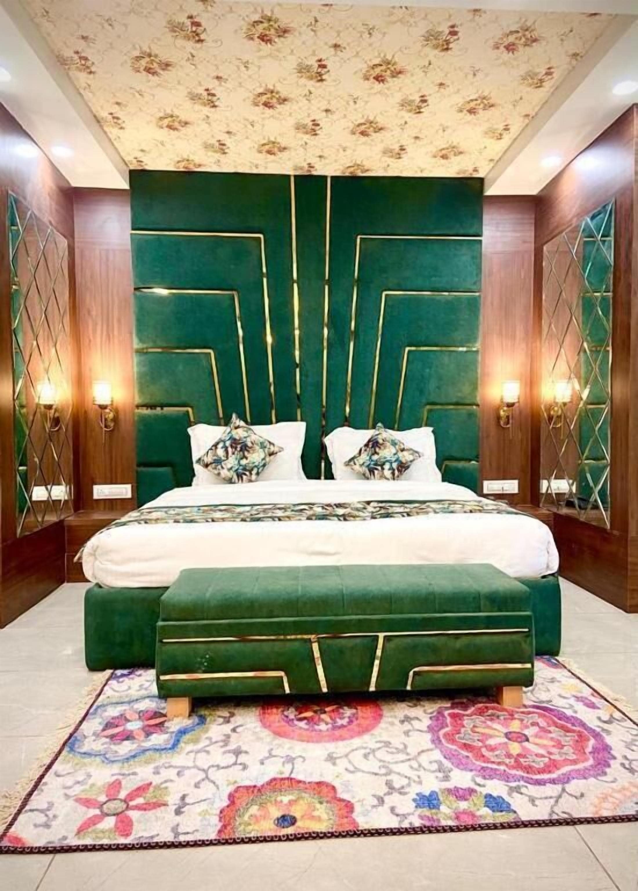 A bedroom with a large bed, green upholstered headboard, and a floral-patterned rug.