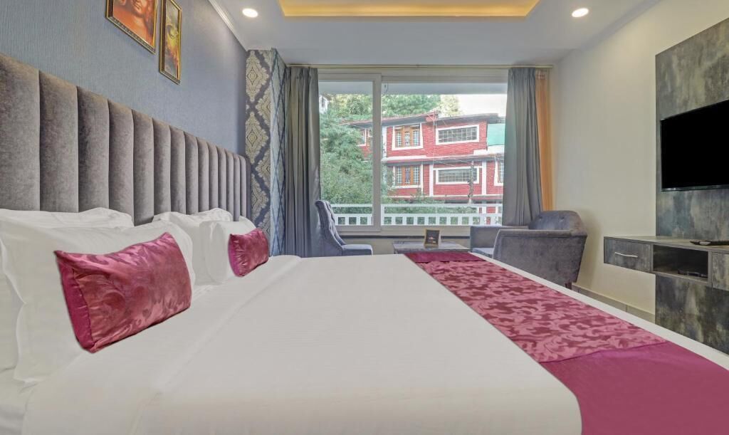 A hotel room with a large bed, a TV, and a view of a building outside.
