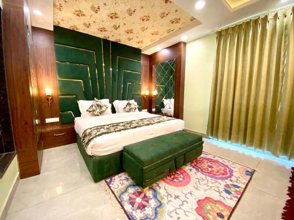 A bedroom with a large bed, a green upholstered bench, a patterned rug, and a decorative ceiling.