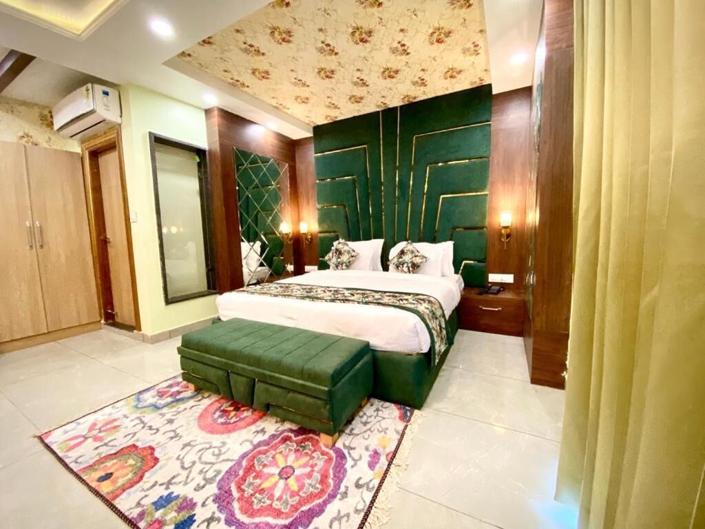 Een slaapkamer met een groot bed, een groene gestoffeerde bank, een getextureerd vloerkleed en een decoratief plafond.