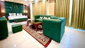A modern hotel room with a green sofa set, a large bed, and a chandelier.