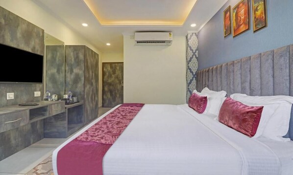 A modern hotel room with a large bed, a vanity with a mirror, and a flat-screen TV mounted on the wall.