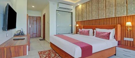 A hotel room with a large bed, a desk with a television, and a wooden headboard.