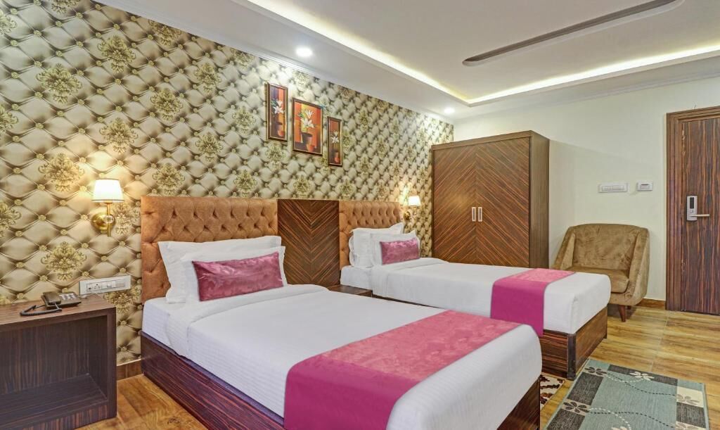 A hotel room with two beds, a large wardrobe, a chair, and a patterned wall.