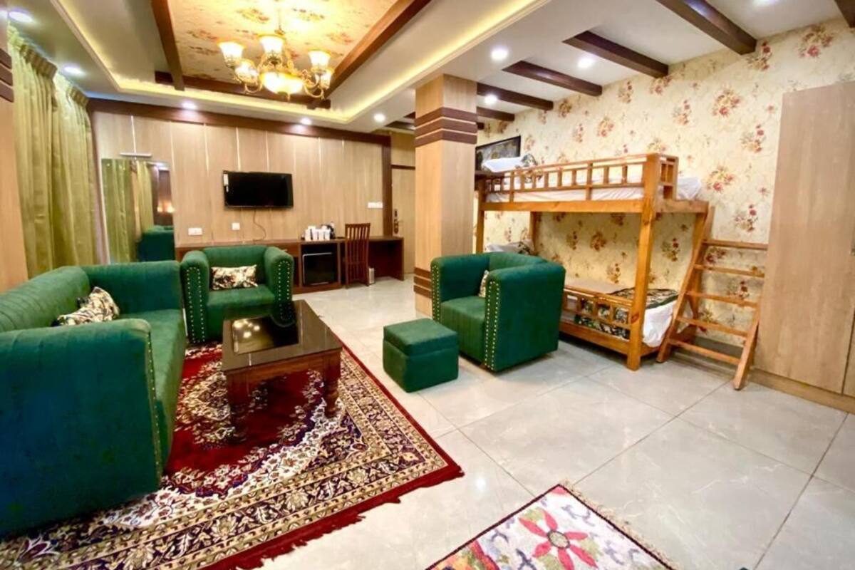 A living room with green sofas, a coffee table, a red patterned rug, a bunk bed, and a television on the wall.