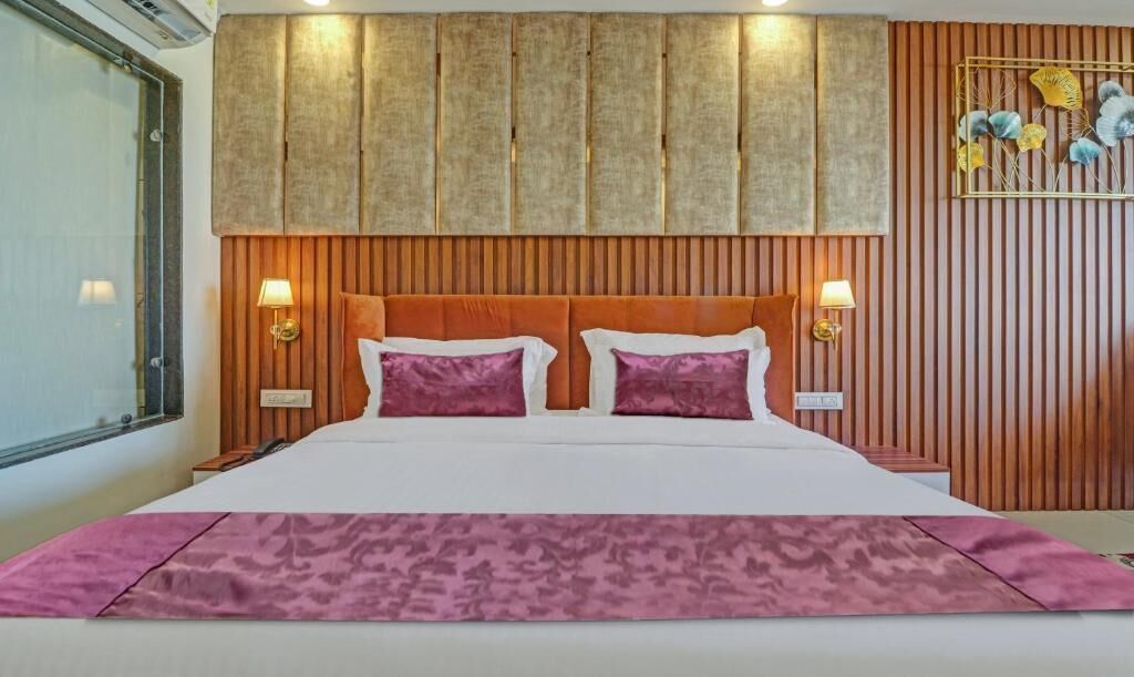 A hotel room with a large bed, wooden headboard, two bedside lamps, and a decorative wall piece.