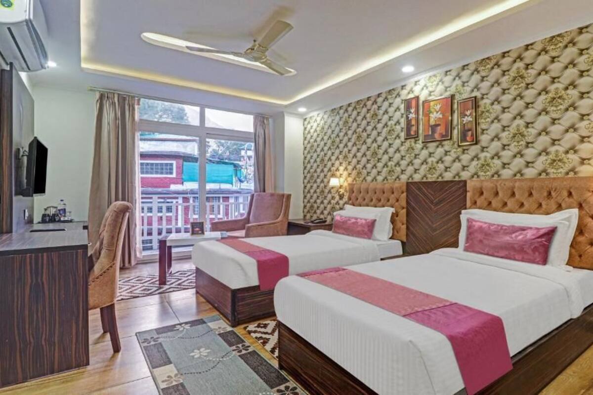A hotel room with two beds, a desk, a chair, and a balcony with a view.