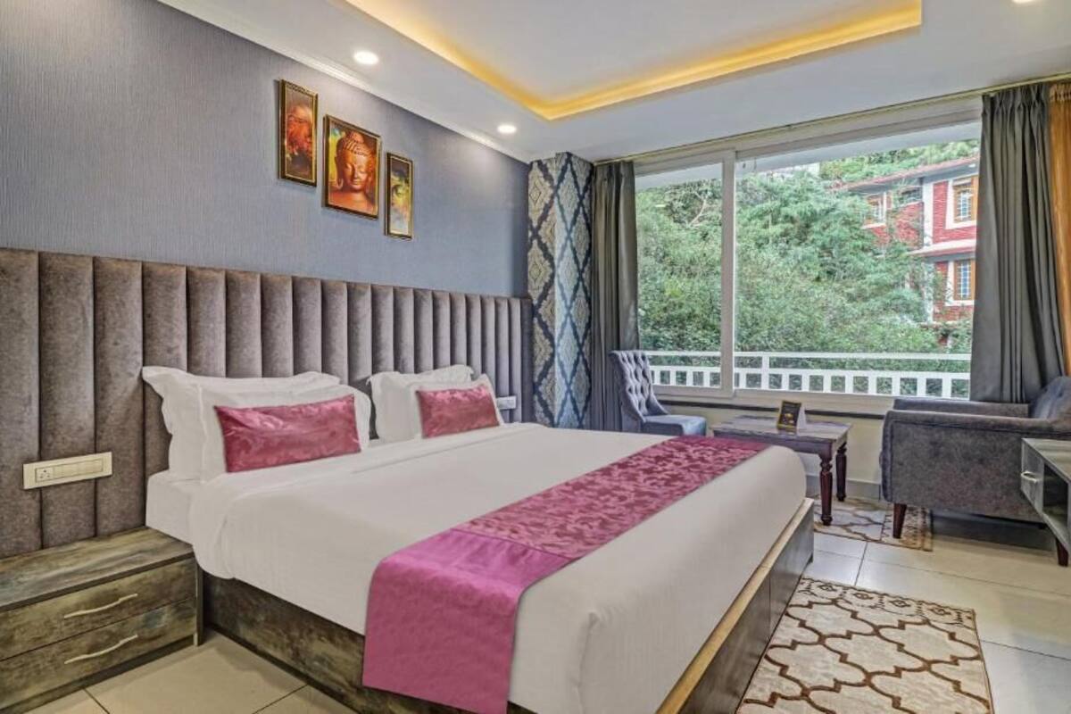 A hotel room with a large bed, a desk, and a view of greenery outside.