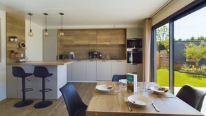 Una cocina moderna con armarios de madera, un comedor con mesa de madera y sillas negras, y un gran ventanal con vistas al jardín.