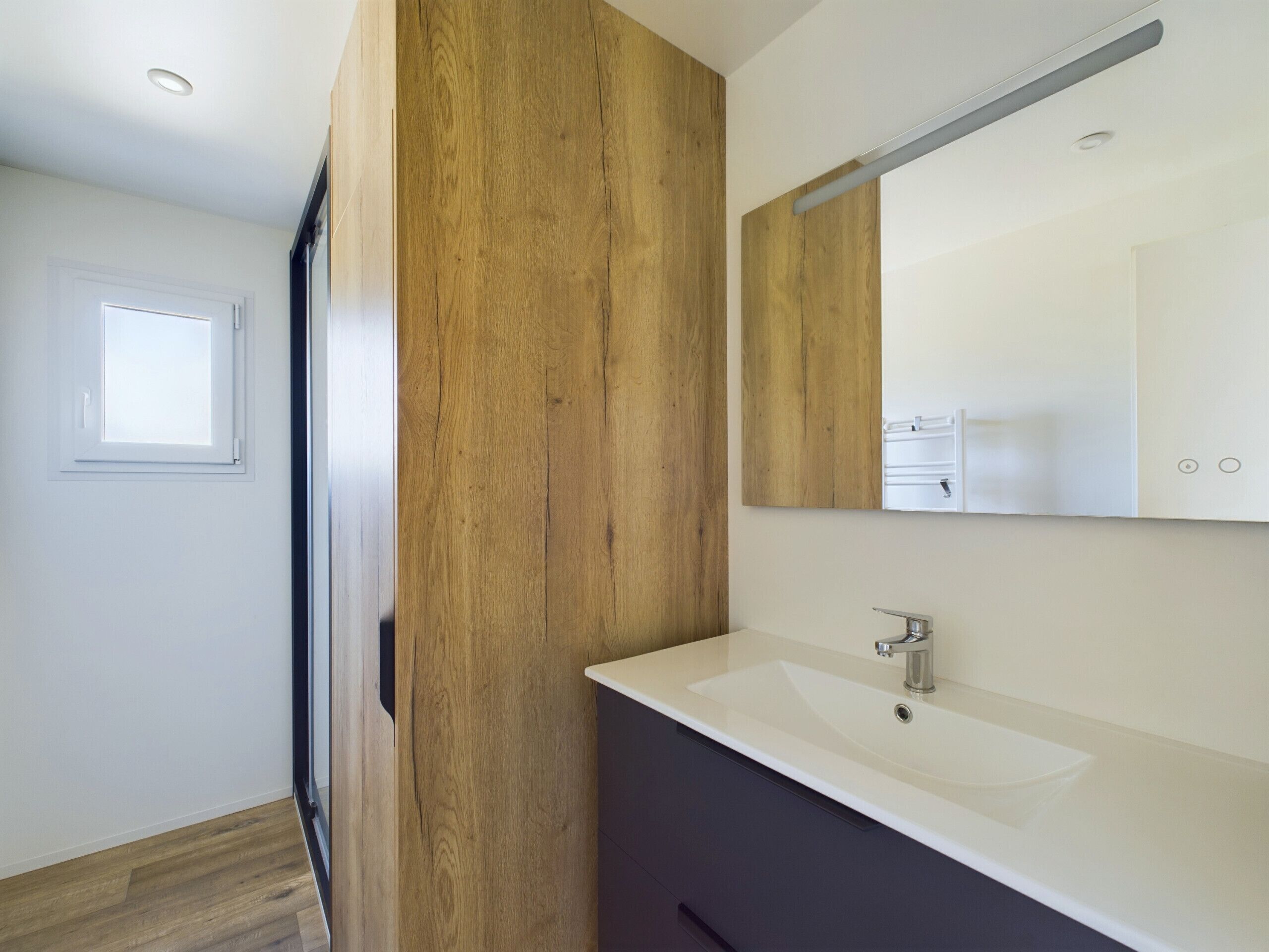 A modern bathroom with a wooden accent wall, a white sink, and a mirror above it.