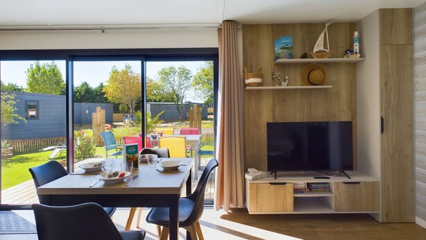 Una sala de estar moderna con un televisor grande, estanterías de madera y un comedor con mesa y sillas.