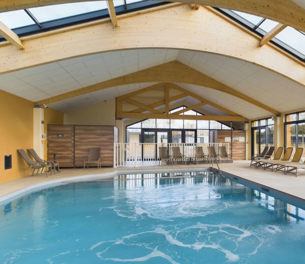 An indoor swimming pool with a wooden ceiling and large windows.
