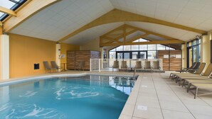 Una piscina interior con techo alto y luz natural proveniente de tragaluces.