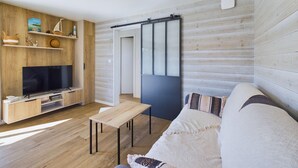Una sala de estar moderna con una televisión de pantalla plana, estanterías de madera, un divisor corredizo y un sofá con cojines estampados.