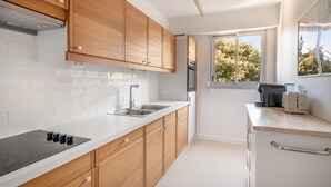 A modern kitchen with wooden cabinets, a white countertop, a built-in oven, and a window providing natural light.