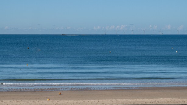 A beach with a clear view of the ocean and distant wind turbines.