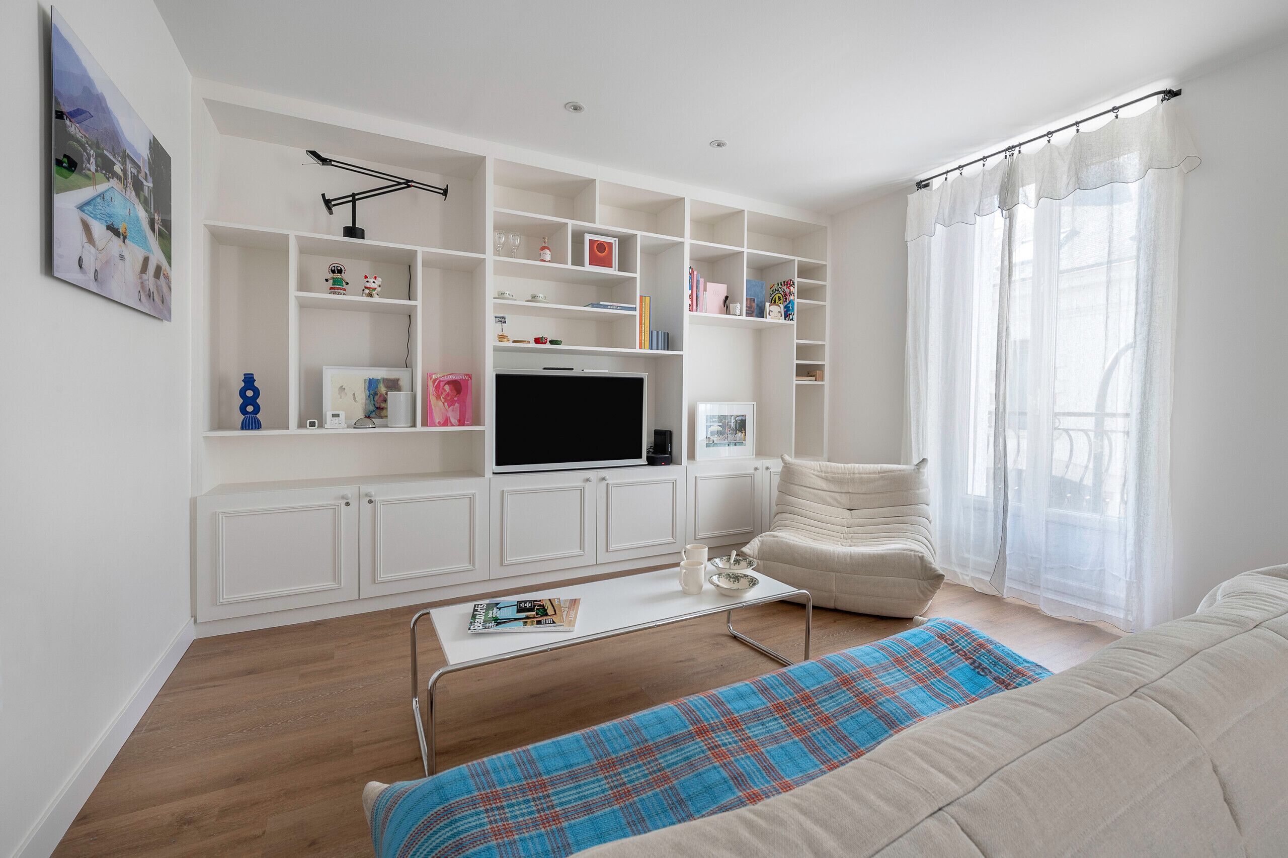 A modern living room with a flat-screen TV, white shelving, a comfortable sofa, and a coffee table.
