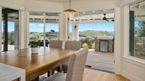 Uma sala de jantar com mesa e cadeiras de madeira, uma luminária pendente e vista para o exterior.