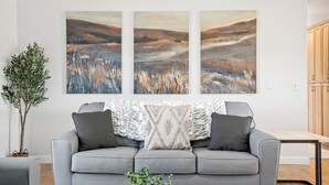 A living room with a grey sofa, a coffee table with a plant, and three abstract paintings on the wall. - Hilltop Guest House w/spectacular vineyard views! (Paso Robles)