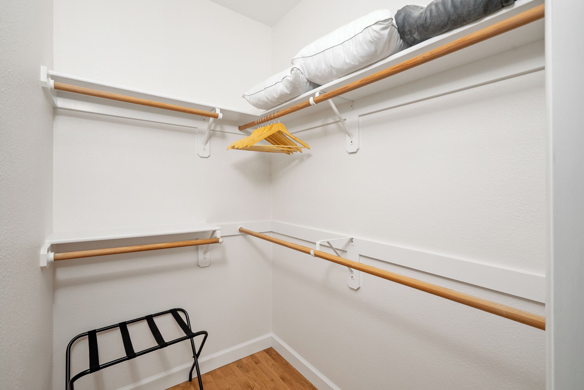 A walk-in closet with multiple wooden shelves and a black metal rack.
