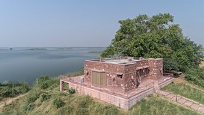 A stone building with a flat roof, a staircase, and a view of a lake. - Narsingh Bagh Resort (Bari)