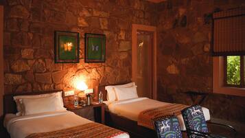 A room with two beds, a stone wall, a ceiling fan, a window with a view, and framed artwork on the wall.