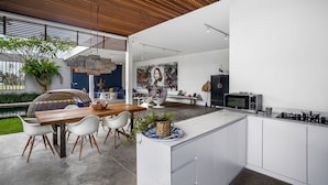 A modern kitchen with a central island, white cabinetry, and a dining area with a wooden table and white chairs. - Loft Volcano by Alfred in Bali - Stylish 2 BR Loft w Pool Garden Ricefields View (Ubud)
