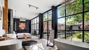 A modern bathroom with a large bathtub, a round sink, and a shower area. There is a large window providing a view of the outdoors. - Loft Volcano by Alfred in Bali - Stylish 2 BR Loft w Pool Garden Ricefields View (Ubud)